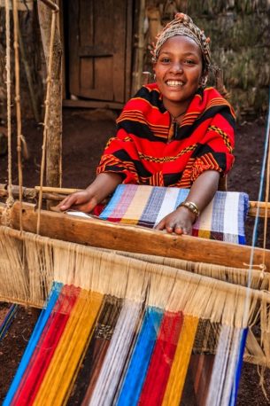 Young African woman from Dorze tribe weaving colorful traditional scarf in the village close to Arba Minch town, southern Ethiopia, Africa.